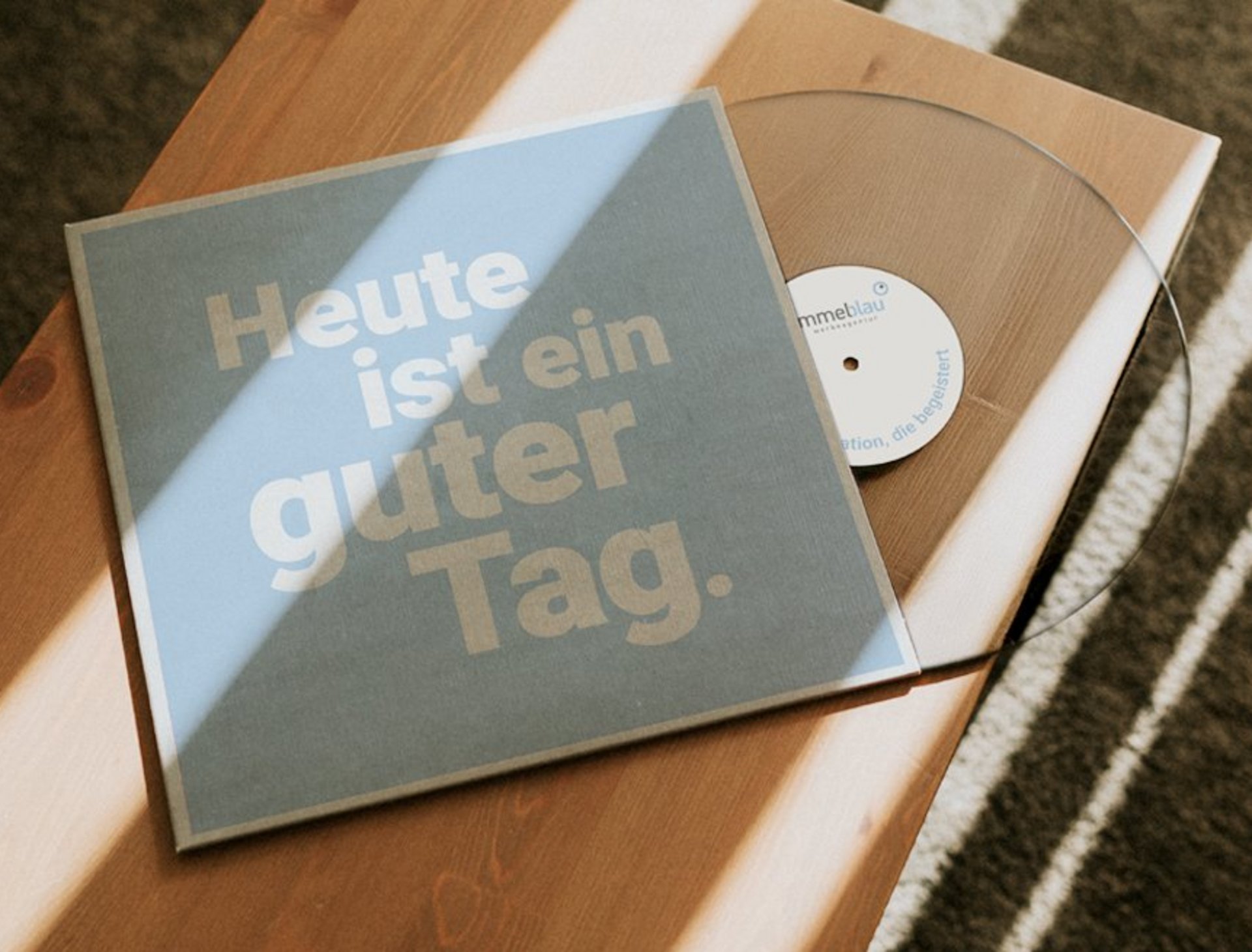Vinylplatte mit dem Covertext «Heute ist ein guter Tag.» auf einem Holztisch, Vynil von Himmelblau, im Sonnenlicht fotografiert.