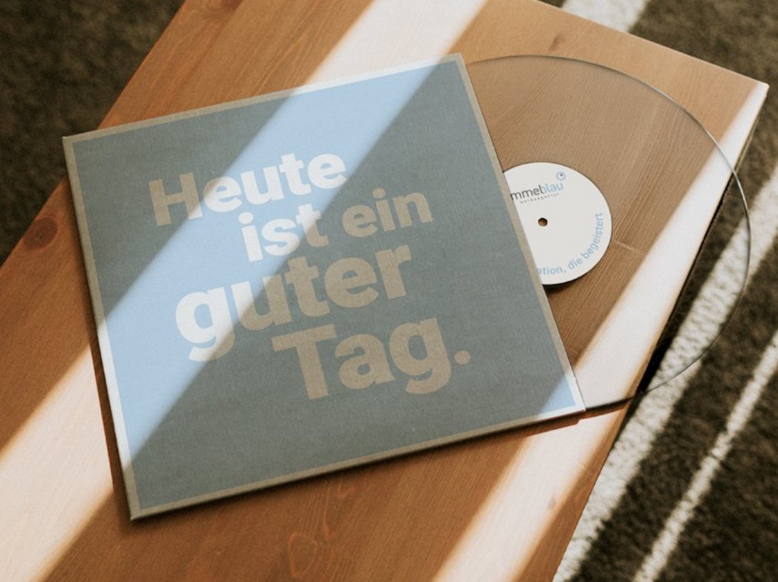 Vinylplatte mit dem Covertext «Heute ist ein guter Tag.» auf einem Holztisch, Vynil von Himmelblau, im Sonnenlicht fotografiert.